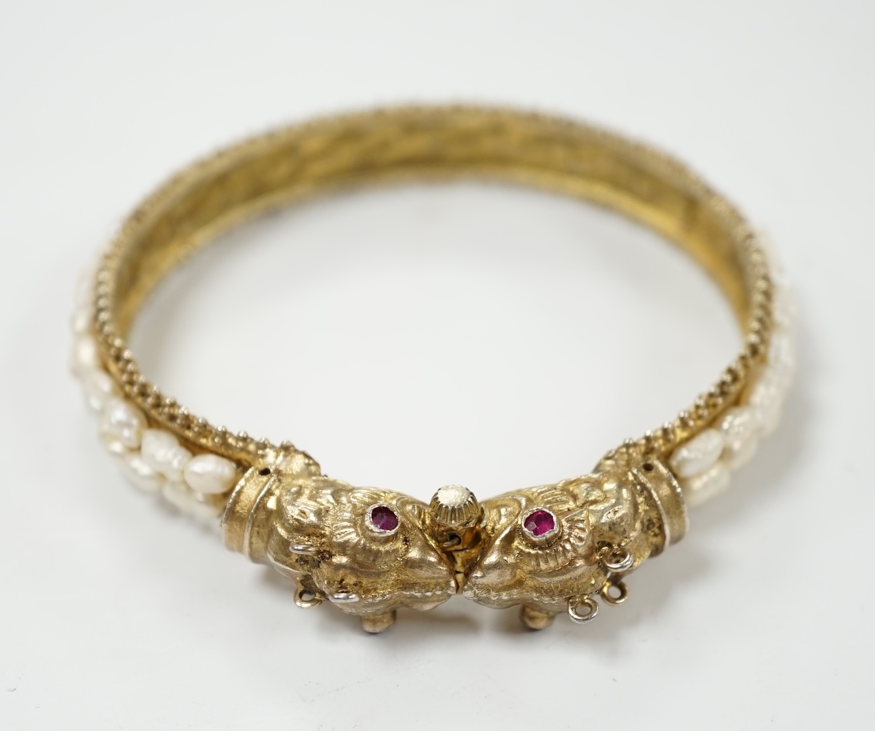 A Chinese? gilt white metal and freshwater pearl cluster set hinged bangle, with red stone eyes. Condition - fair